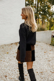 Jupe en daim à damier portée par une femme, vue de profil, bottes noires, mur blanc