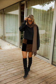 Jupe en daim à damier portée par une femme, silhouette entière, bottes noires, terrasse en bois