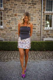 Jupe courte à sequins portée par une femme, silhouette entière, mur en pierre, top bleu marine