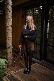 Jupe satinée à dentelle portée par une femme, silhouette entière, collants, bottines noires