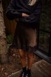 Jupe satinée à dentelle portée par une femme, vue rapprochée, pull noir, jupe satinée marron, bottines
