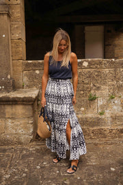 Jupe longue tie-dye fendue portée par une femme, silhouette entière, mur en pierre, panier