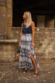 Jupe longue tie-dye fendue portée par une femme, silhouette entière, mur en pierre, fente