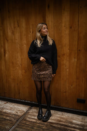 Jupe léopard effet daim portée par une femme, silhouette entière, mur en bois, collants