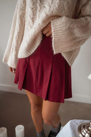 Jupe plissée à zip portée par une femme, vue rapprochée, pull crème, bottines