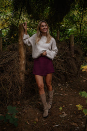 Jupe-short zippée sur le côté porté par une femme, silhouette entière, forêt, bottes beiges