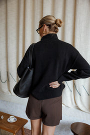 Jupe-short à carreaux porté par une femme, vue de dos, pull noir, mains sur les hanches