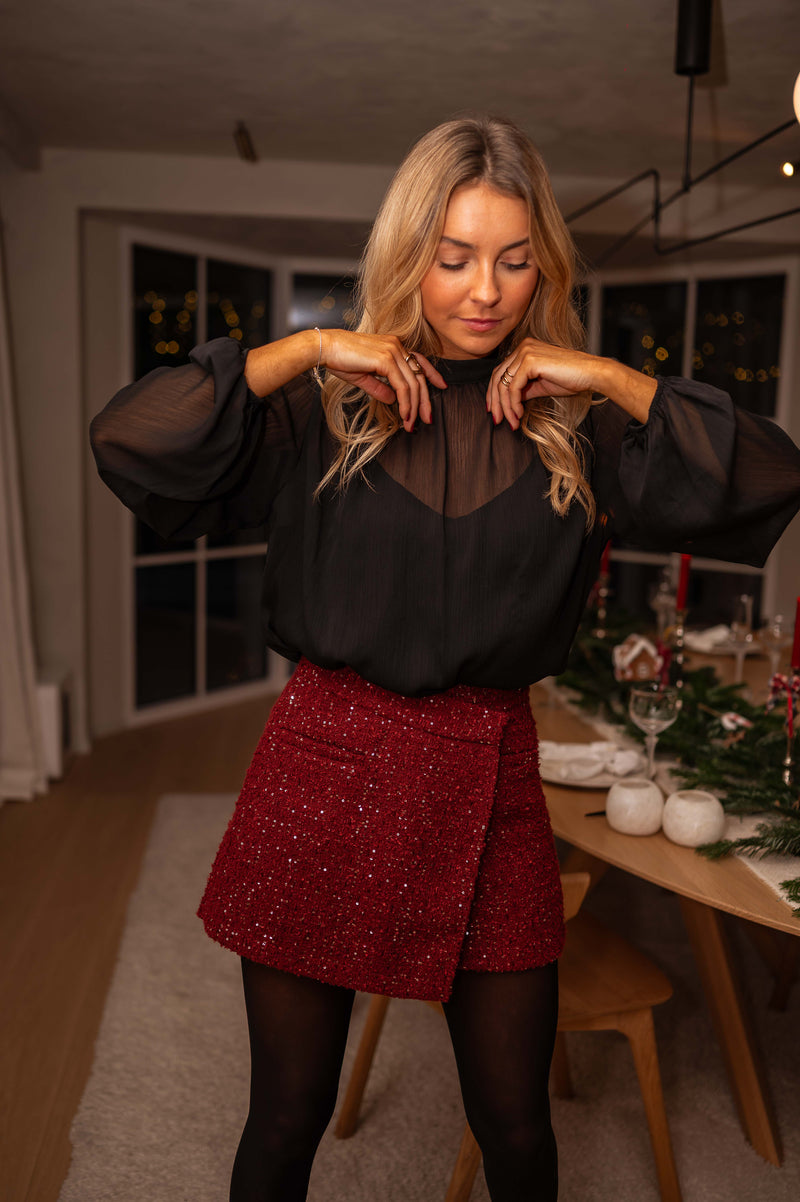 Jupe-short en tweed brillant bordeaux porté par une femme, vue de trois-quarts, blouse noire, table dressée