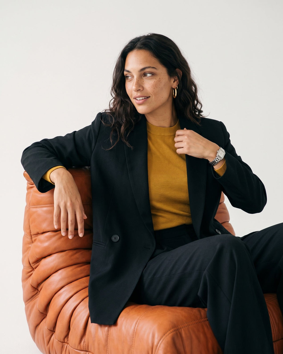 Blazer croisé à coupe ajustée porté par une femme, assise, fauteuil en cuir, haut moutarde