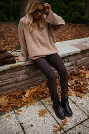 Legging moulant à fente porté par une femme, assise, muret, pull beige