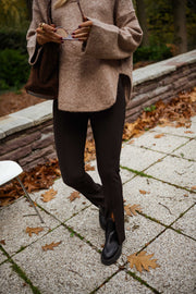 Legging moulant à fente porté par une femme, silhouette entière, pull beige, pavés