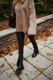 Legging moulant à fente porté par une femme, silhouette entière, pull beige, bottines, muret