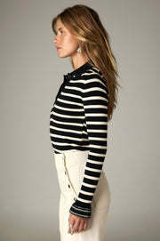 Pull polo noir à rayures écrues et manches longues, porté de profil