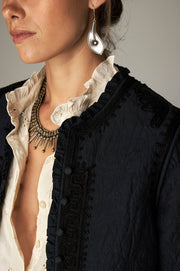 Détail de l’encolure et des bordures décorées de la veste sombre.