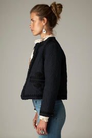 Veste courte sombre à manches longues et bordures décorées, vue de profil.