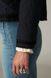 Détail de la manche sombre à motifs ton sur ton et du poignet froncé de la veste.