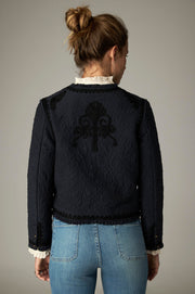 Veste courte sombre vue de dos, avec un grand motif décoratif ton sur ton.