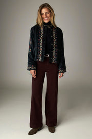 Vue d’ensemble de la veste courte sombre à broderies multicolores, portée de face.
