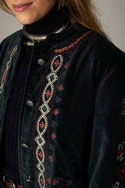 Détail de l’encolure ronde, des boutons et des broderies multicolores de la veste sombre.