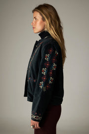 Vue de profil de la veste sombre, avec broderies multicolores sur la manche et le poignet.