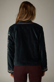 Dos de la veste sombre, avec bordure brodée à l’encolure et motifs multicolores sur les manches.