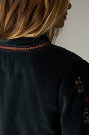 Détail de la bordure brodée au dos de l’encolure de la veste sombre.