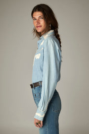 Chemise bleu clair à manches longues et poignets décorés, portée de profil
