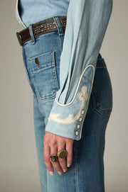 Détail du poignet à motifs crème, passepoil et boutons de la chemise bleu clair