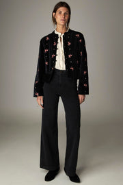 Veste noire à fleurs roses et manches longues, portée ouverte dans une vue en pied.
