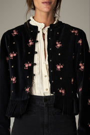 Détail du devant boutonné, des fleurs roses et du bas plissé de la veste noire.