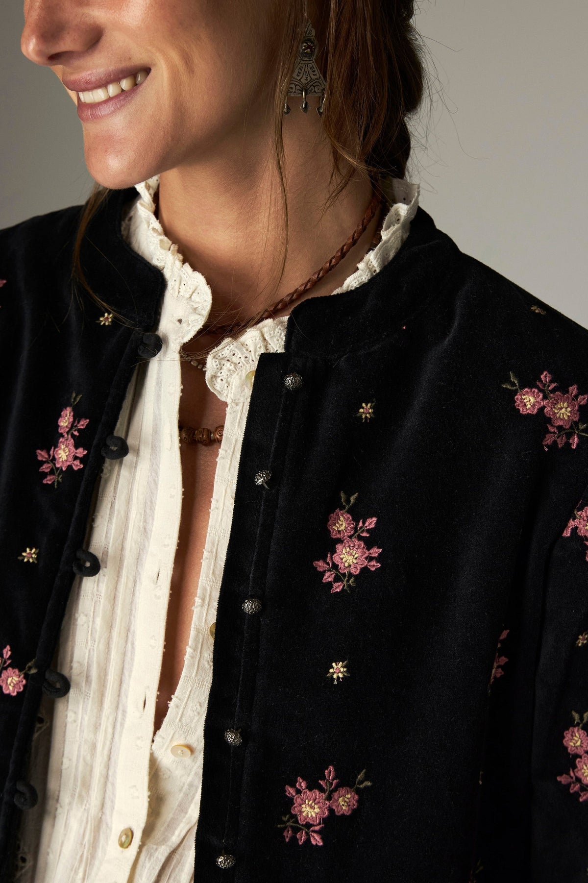 Détail d’une veste noire à motifs de fleurs roses et fermeture boutonnée.