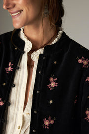 Détail d’une veste noire à motifs de fleurs roses et fermeture boutonnée.