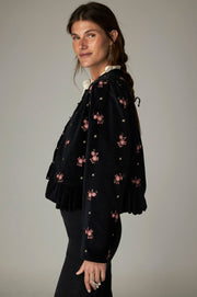 Veste noire à fleurs roses et bas plissé, portée de profil.