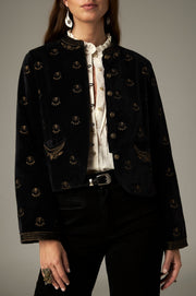 Veste noire à petits motifs dorés, col rond et poches devant, portée ouverte.