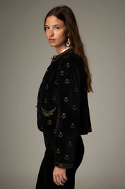 Vue de profil de la veste noire à motifs dorés, avec poche devant et manches longues.