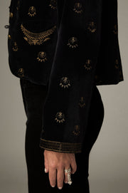 Détail des broderies dorées sur la manche, le poignet et la poche de la veste noire.
