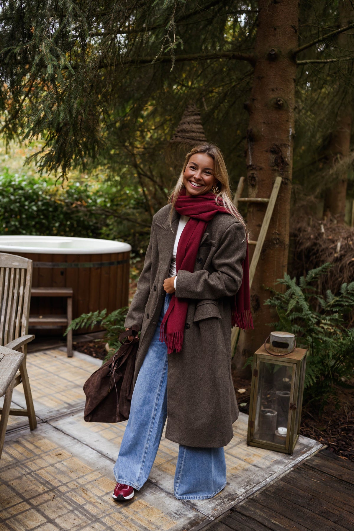 Manteau long doublé à épaulettes taupe porté par une femme, vue de face, terrasse, écharpe bordeaux