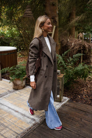 Manteau long doublé à épaulettes taupe porté par une femme, vue de trois-quarts, terrasse, bottines rouges