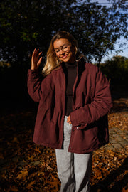 Manteau ample imperméable bordeaux porté par une femme, vue de face, sous-bois, col relevé