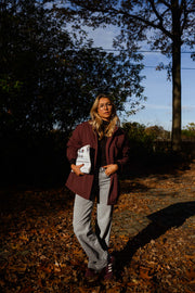 Manteau ample imperméable bordeaux porté par une femme, vue de face, feuilles d'automne, livre blanc