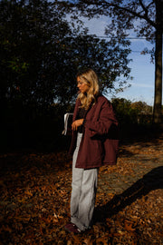 Manteau ample imperméable bordeaux porté par une femme, vue de dos, sous-bois, jean gris