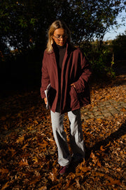 Manteau ample imperméable bordeaux porté par une femme, vue de face, feuilles d'automne, jean gris