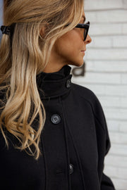 Manteau à col montant boutonné noir porté par une femme, vue rapprochée, col montant, boutons