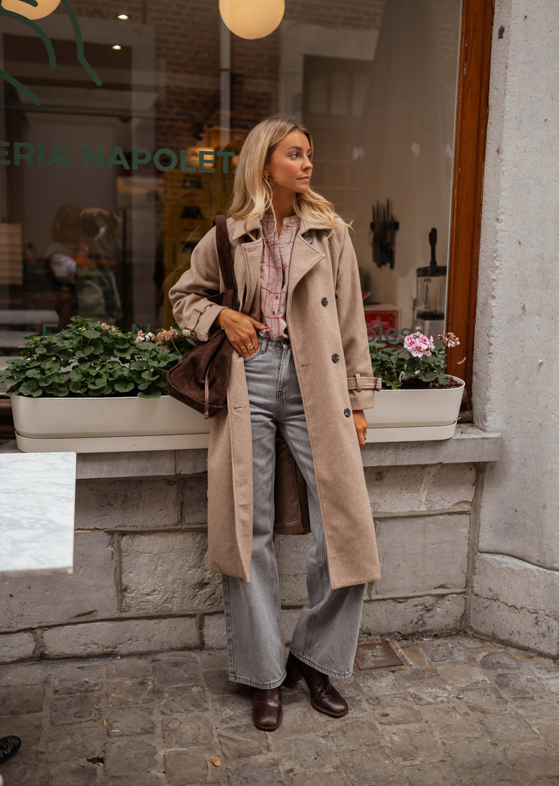 Manteau long ceinturé doublé taupe porté par une femme, silhouette entière, vitrine, sac