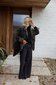 Manteau à carreaux doublé porté par une femme, vue de face, dalles claires, sac noir
