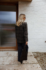 Manteau à carreaux doublé porté par une femme, vue de dos, porte vitrée, cheveux blonds