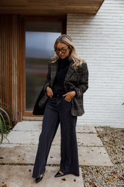 Manteau à carreaux doublé porté par une femme, vue de face, mur blanc, sac noir tenu à la main