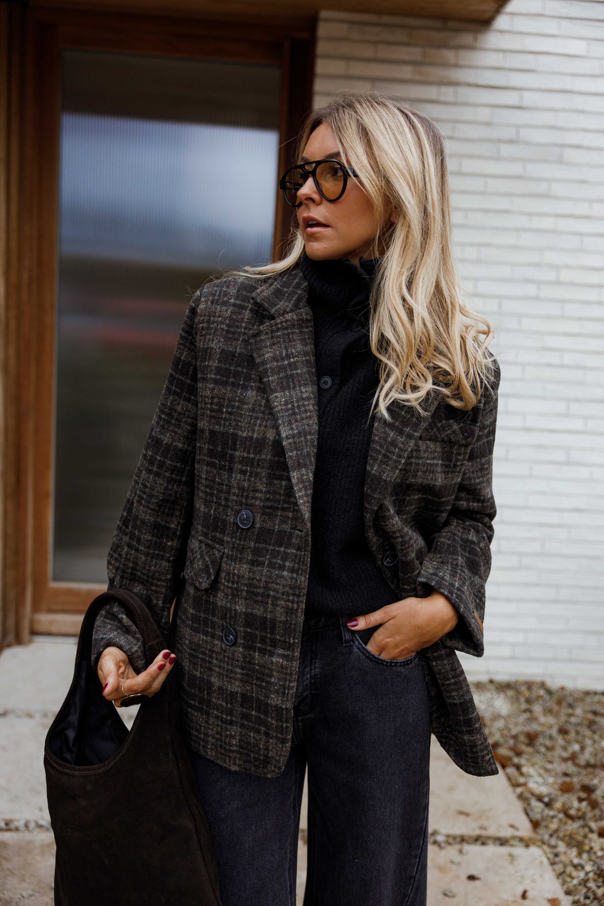 Manteau à carreaux doublé porté par une femme, vue de trois-quarts, mur blanc, lunettes de soleil