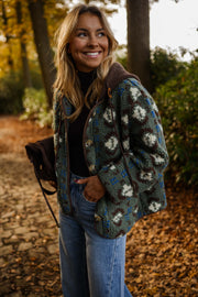 Manteau polaire à capuche amovible porté par une femme, vue de face, allée pavée, sourire