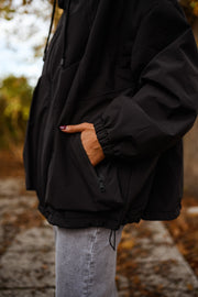 Manteau à capuche imperméable noir porté par une femme, vue rapprochée, poche, jean gris